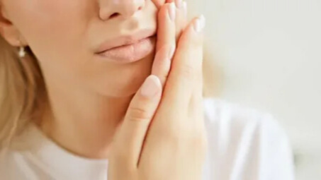 Young woman holding her cheek in discomfort after wisdom teeth removal, illustrating the healing process and recovery period.