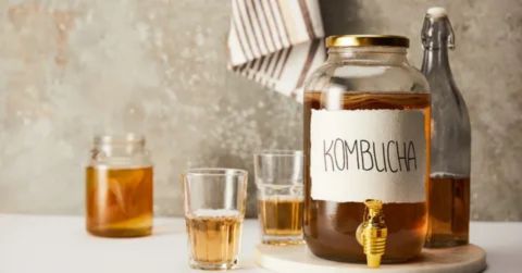A glass jar of kombucha with glasses on a table, representing the benefits of drinking kombucha in the evening as a healthy, soothing nighttime beverage.