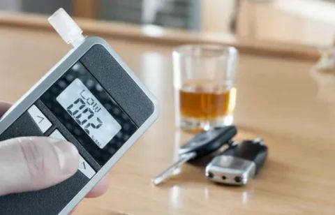 A close-up of a digital breathalyzer device displaying a low BAC reading, with car keys and a glass of whiskey in the blurred background, illustrating the detection of alcohol for driving safety.