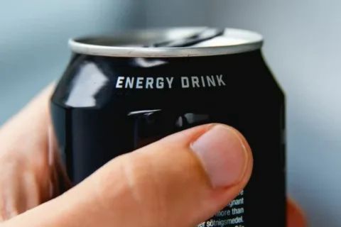 Close-up shot of a hand holding a black energy drink can, highlighting the source of high caffeine and sugar content that can trigger acne flare-ups in vulnerable individuals.