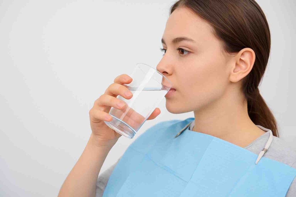 Woman carefully sipping a glass of water after dental filling, representing safe drinking habits and post-filling recovery tips.