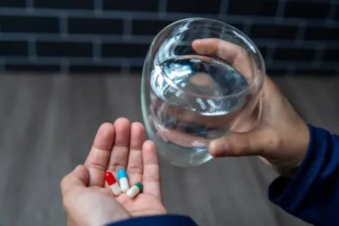 Person holding pills and a glass of water, highlighting the risks of drinking alcohol while taking Vyvanse.