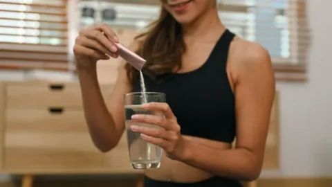 Pregnant woman’s hand stirring a glass of collagen drink, representing guidance on safe collagen intake during pregnancy and the importance of moderation.