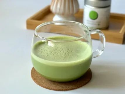 Clear glass cup filled with freshly prepared matcha green tea on a coaster, illustrating safe daily consumption tips for breastfeeding mothers.