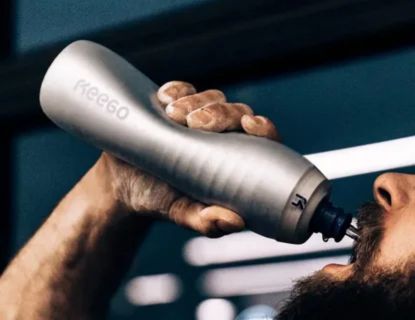 A person drinking from a contoured, stainless steel or metal water bottle with a secure spout, illustrating the recommended container for mixing and consuming creatine on the go.