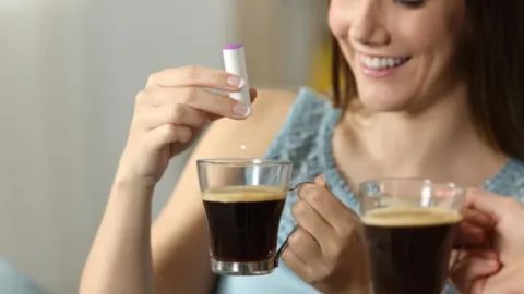 “A woman adding stevia to a cup of black coffee, showing a fasting-friendly drink that supports energy, focus, and fat-burning during intermittent fasting.”