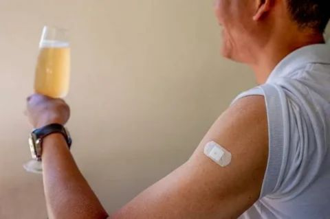 A man holding a glass of alcohol after a medical procedure with a bandage on his arm, representing alcohol safety concerns after stent placement.