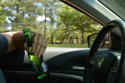 A driver holding a beer bottle inside a parked car, representing Florida’s open container law for drinking in parked vehicles.