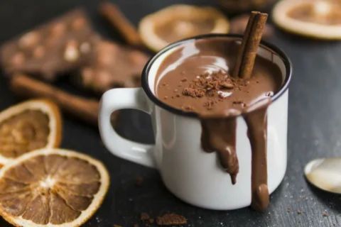 A warm cup of hot chocolate with cinnamon sticks and chocolate drips, creating a soothing drink that may help comfort a sore throat.