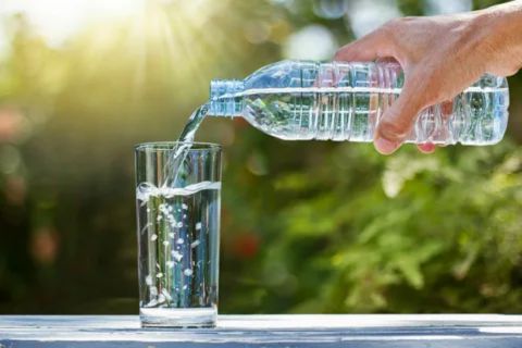 A bottle of water being poured into a glass outdoors, showing the importance of hydration during SUTAB bowel prep.