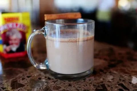 A warm mug of hot chocolate on a table with cinnamon, showing a soothing drink that can help comfort a sore throat and provide relief.