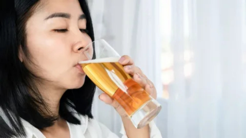 A woman drinking a glass of beer in moderation, illustrating safe alcohol consumption and heart health recommendations after stent placement.