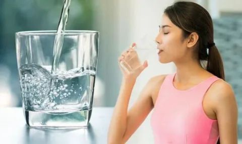 A woman in a pink top taking a drink from a glass of water, with a larger glass of fresh water being poured beside her, symbolizing hydration and its role in managing allergy symptoms.