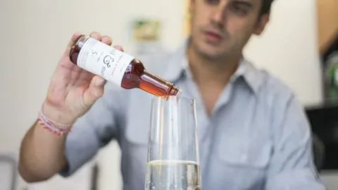 A person pouring an amber-colored liquid from a small bottle into a clear glass, symbolizing the personal choice and mindful approach Quakers take toward consuming alcohol.