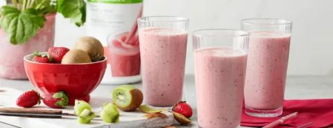 “Strawberry protein shakes in clear glasses with fresh kiwi and strawberries nearby, illustrating that protein drinks are not always the cause of constipation.”