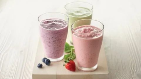 “Three colorful protein smoothies in glasses on a table with fresh berries and spinach, representing how protein drinks may contribute to constipation depending on ingredients.”
