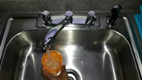 A person filling a cup with tap water from a kitchen sink, illustrating concerns about how safe Jamaica’s tap water is for locals and travelers.