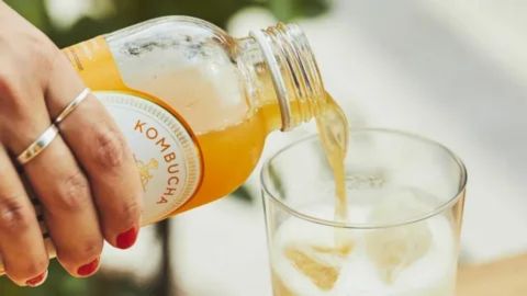 “Hand pouring kombucha into a glass, illustrating considerations for caffeine, alcohol, and probiotics while breastfeeding.”