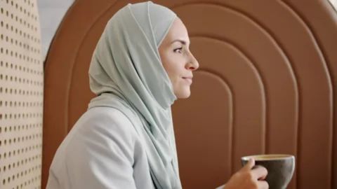 A Muslim woman wearing a hijab peacefully enjoying a cup of coffee, representing that drinking coffee is considered halal and permissible in Islam.