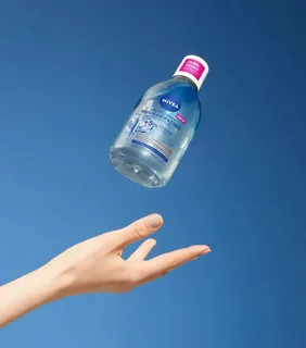 hand catching a bottle of micellar water in mid-air, representing accidental ingestion and highlighting the potential stomach irritation and mild symptoms that can occur if micellar water is swallowed.