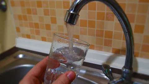 A glass being filled from a kitchen tap, illustrating concerns about tap water safety in Thailand due to aging pipes, rooftop tanks, and inconsistent water infrastructure.