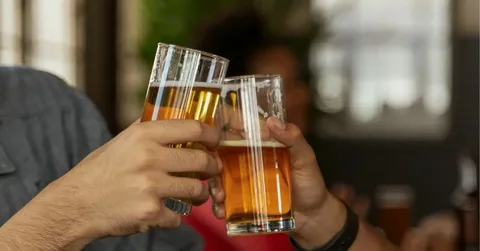 People clinking glasses of beer indoors, representing a common situation where someone may wonder if beer left out for a period of time is still safe to drink.