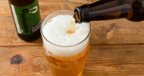 Beer being poured into a glass with foam forming on top, illustrating how temperature, air exposure, and beer type affect whether left out beer remains drinkable.
