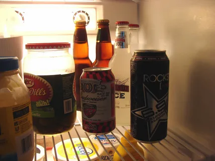 Various bottles and cans of beer sitting inside a refrigerator, illustrating how beer quality and drinkability change when left out at room temperature for several hours or days.